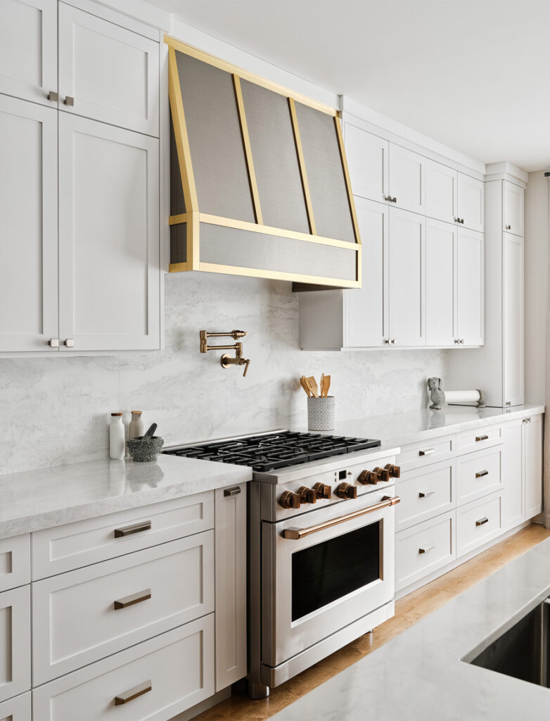 A kitchen with white cabinets and a gold hood above the stove.