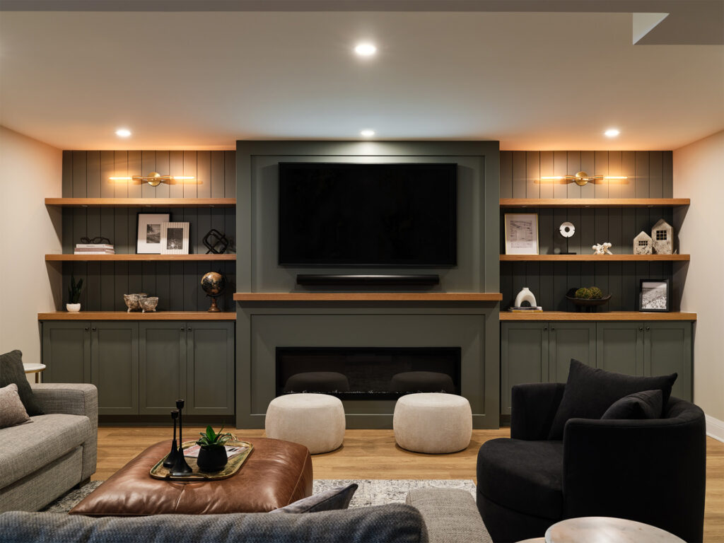 An elegant and modern recreation room featuring a dark olive built-in wall unit with open shelving on either side of a centrally mounted flat-screen television