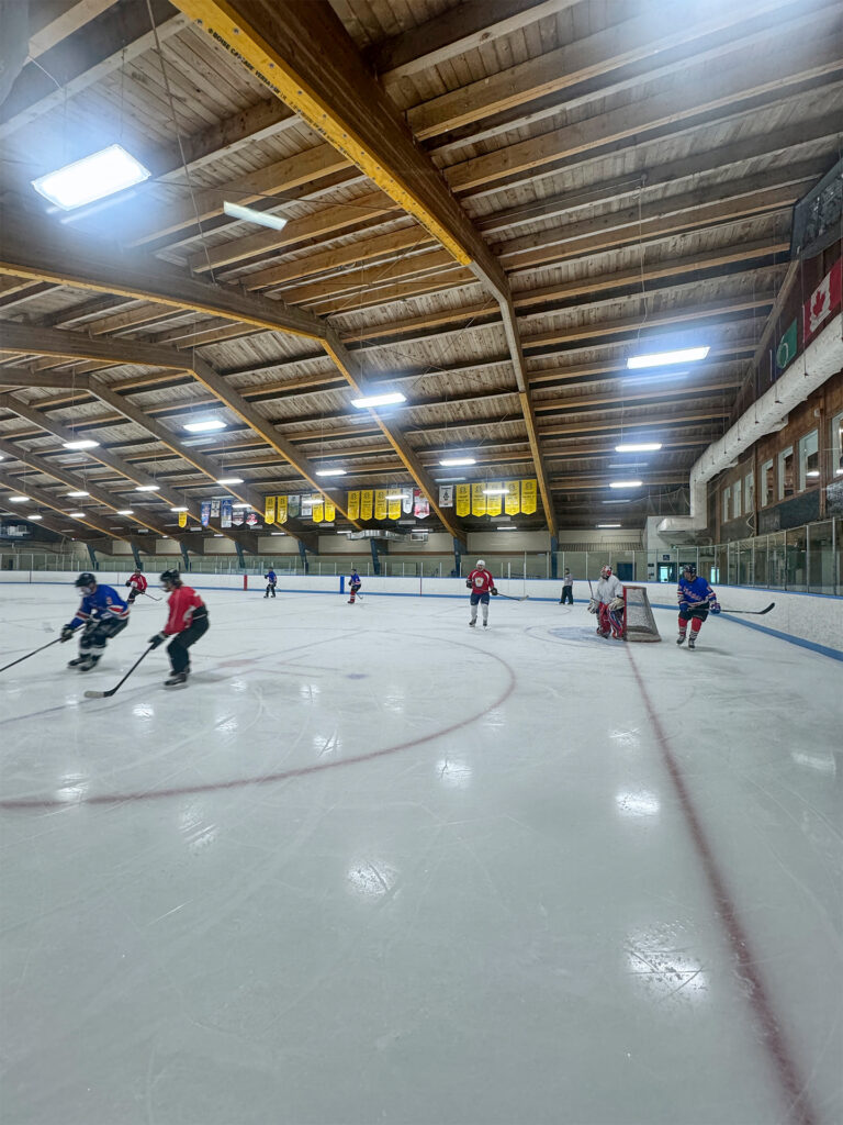 Interior of Fred Barrett Arena during a hockey game, with a wooden arched ceiling and banners hanging overhead