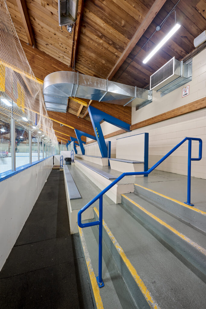 Side view of Fred Barrett Arena's seating with blue railings and exposed wooden ceiling