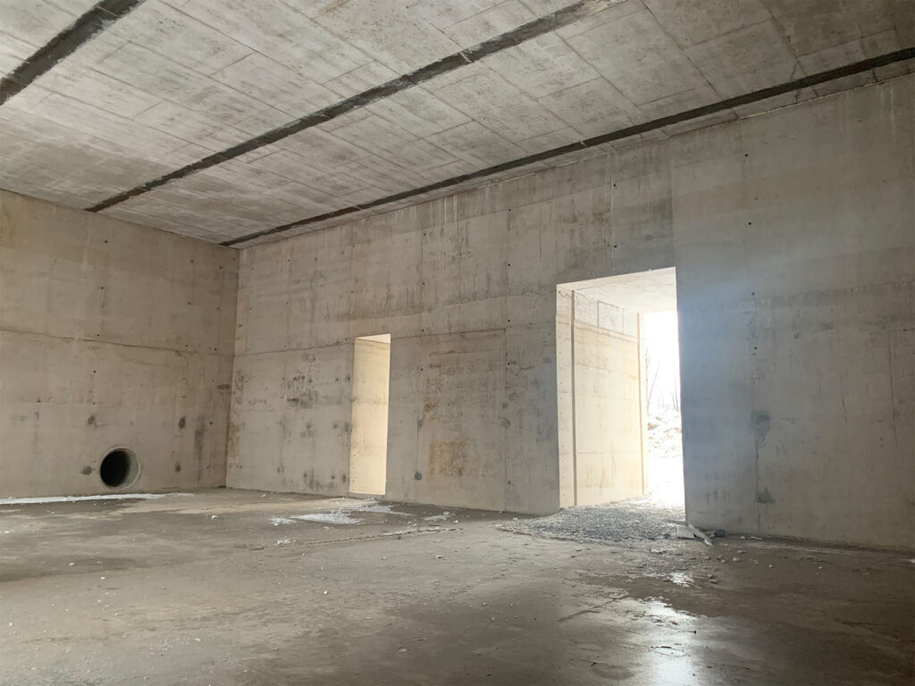 The interior of an under-construction structure with large concrete walls and openings that allow light to stream in