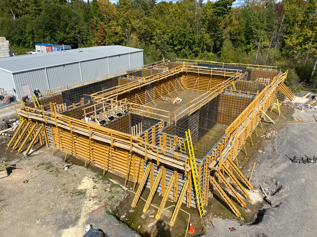 An aerial view of a construction site with wooden scaffolding and rebar frameworks, indicating an early phase of a building's foundation work