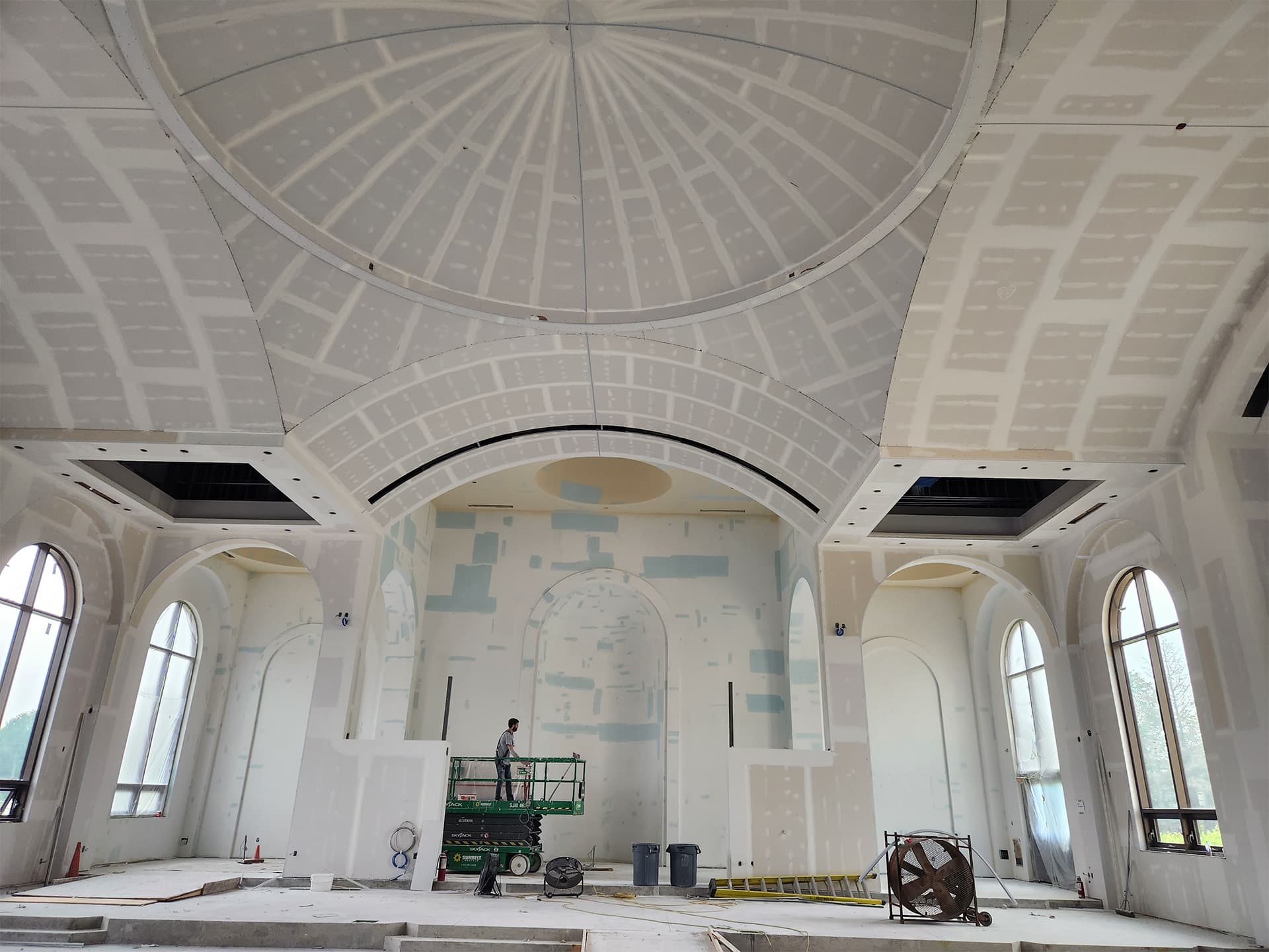 Church interior under renovation with a worker on a lift, featuring a domed ceiling and large arched windows