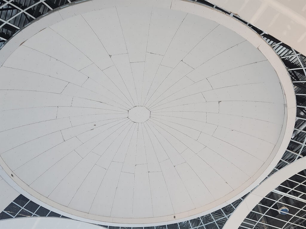 View of an unfinished white dome ceiling with radial lines converging at the center, surrounded by a structural framework, suggesting a building under construction