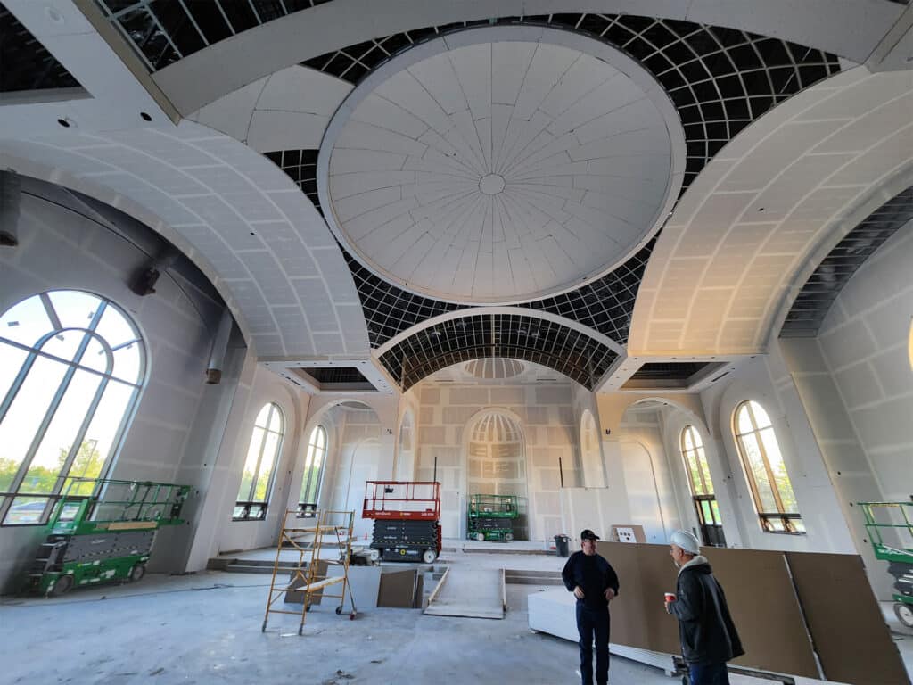 Interior of St. Joseph Orthodox Church under construction, featuring arched windows and a domed ceiling, with workers and construction equipment.