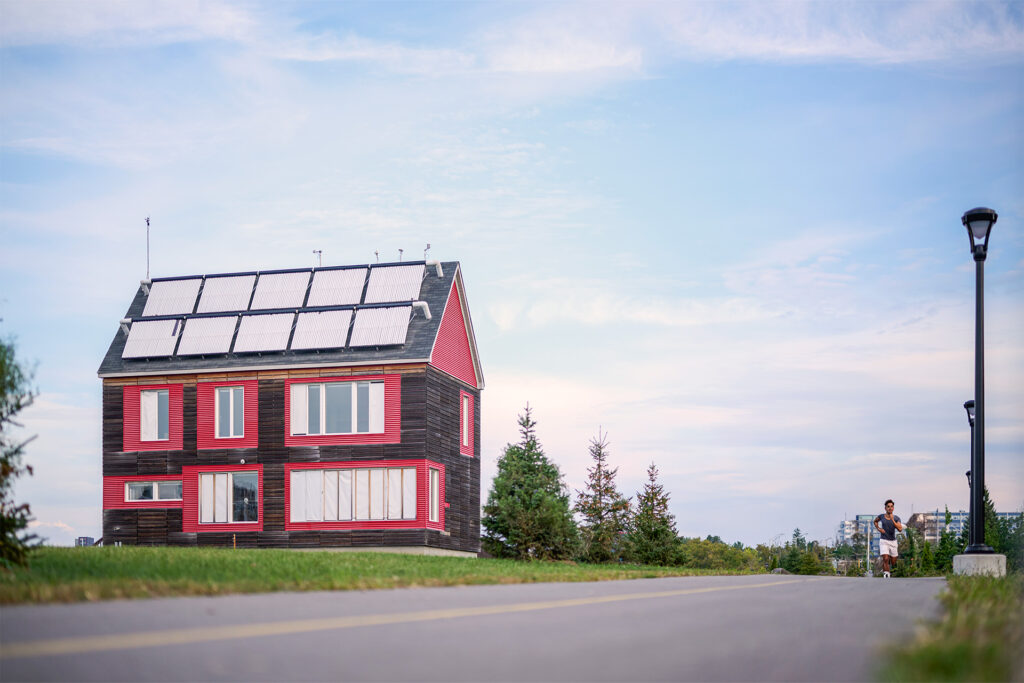 A modern two-story house with red accents and a solar panel installation on the roo
