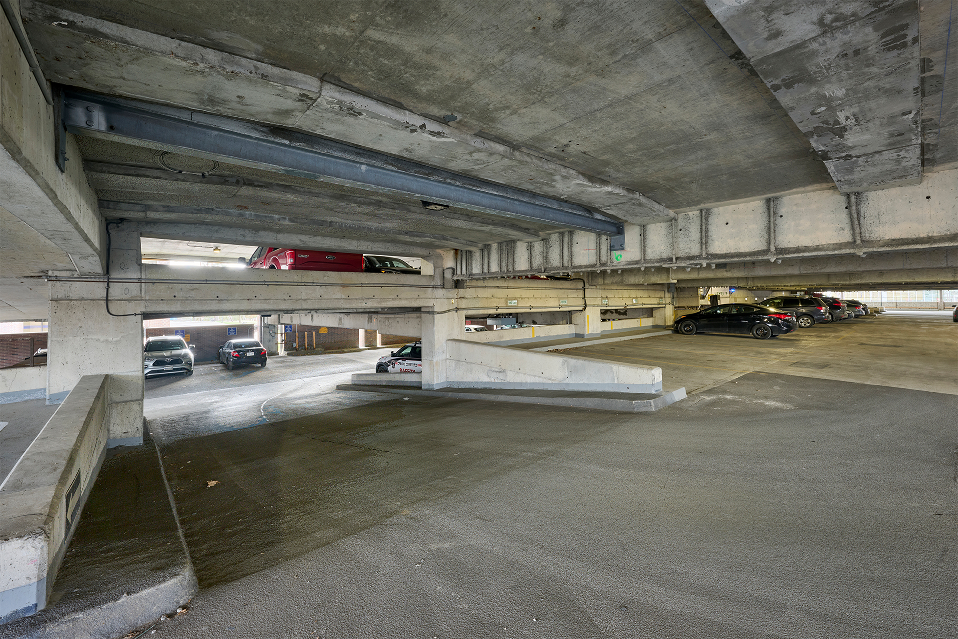 Interior of Carleton University's Parking 9 showing vehicles parked on multiple levels, concrete pillars, and overhead beams