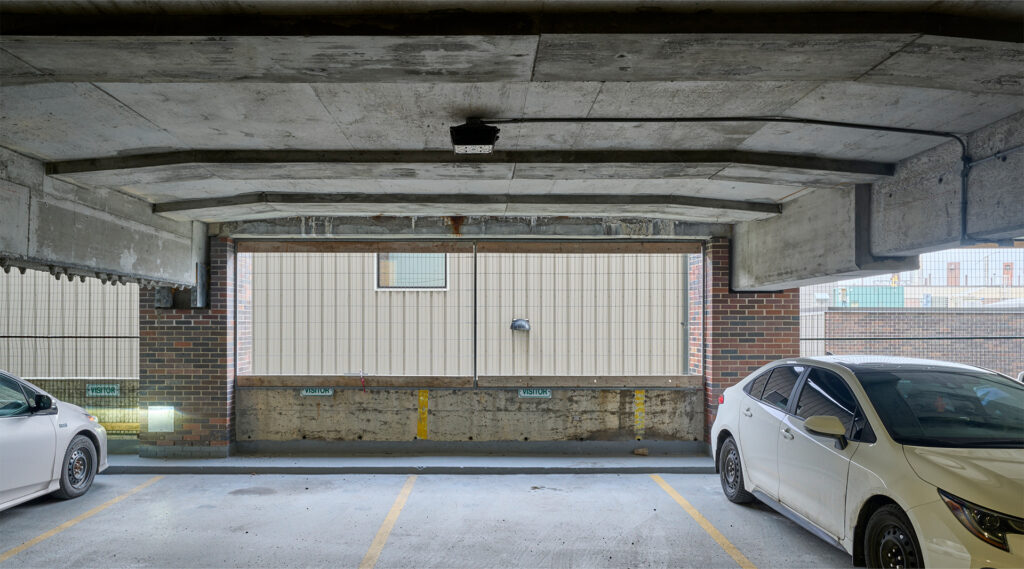 Designated visitor parking spots at the Carleton University Parking 9, featuring a concrete structure with a brick wall and tiled section