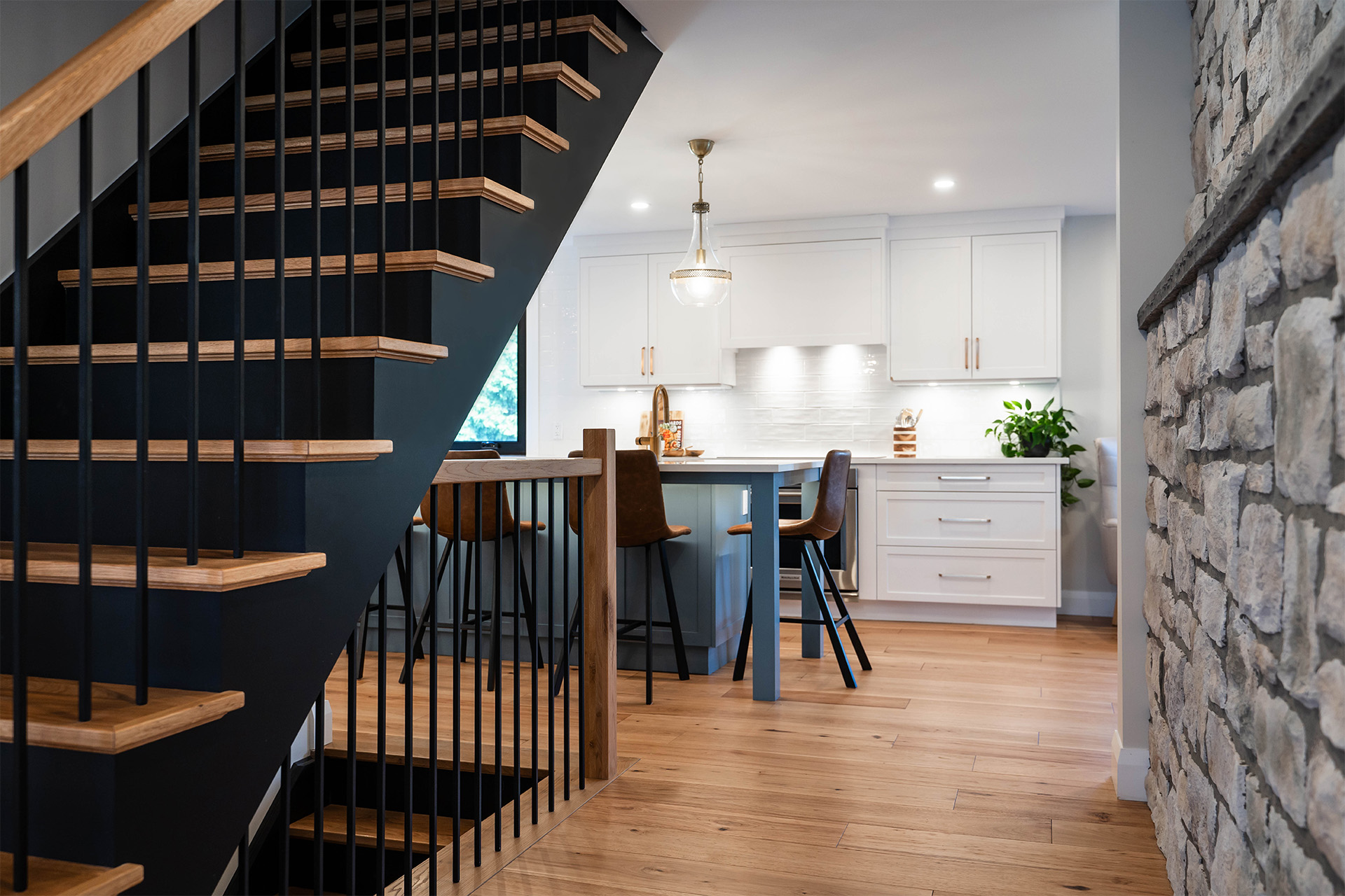 A modern kitchen with white cabinetry and a stone accent wall beside a black staircase with wooden steps
