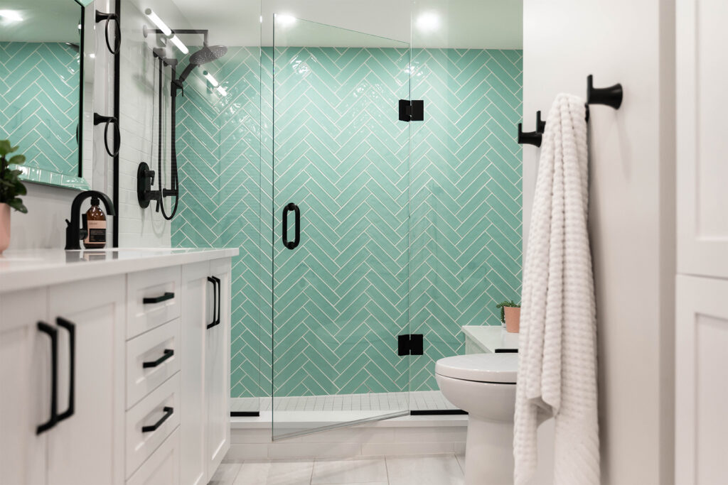 A modern bathroom featuring herringbone-patterned teal tiles, glass shower enclosure, and sleek black fixtures