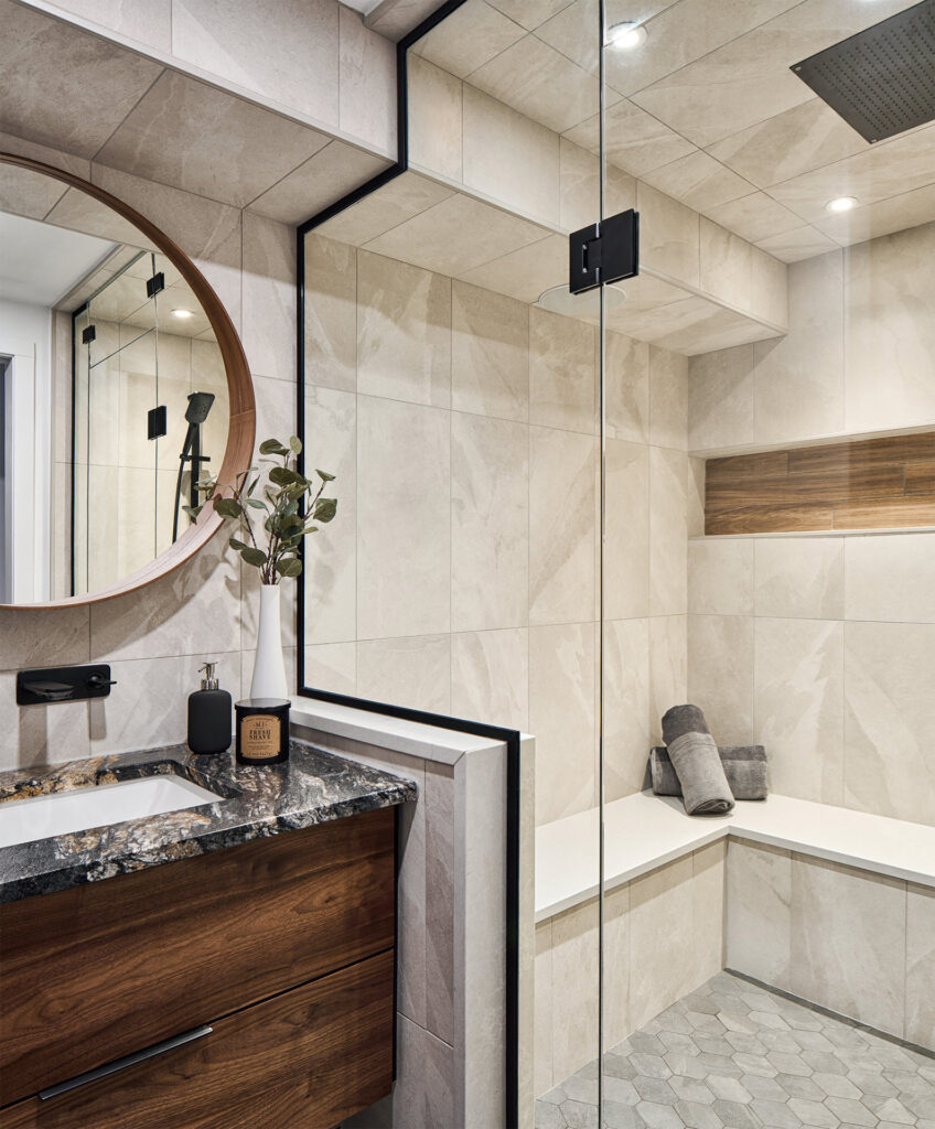 Modern bathroom interior featuring a wooden vanity with a granite countertop, a round mirror, and a spacious walk-in shower with beige tiles