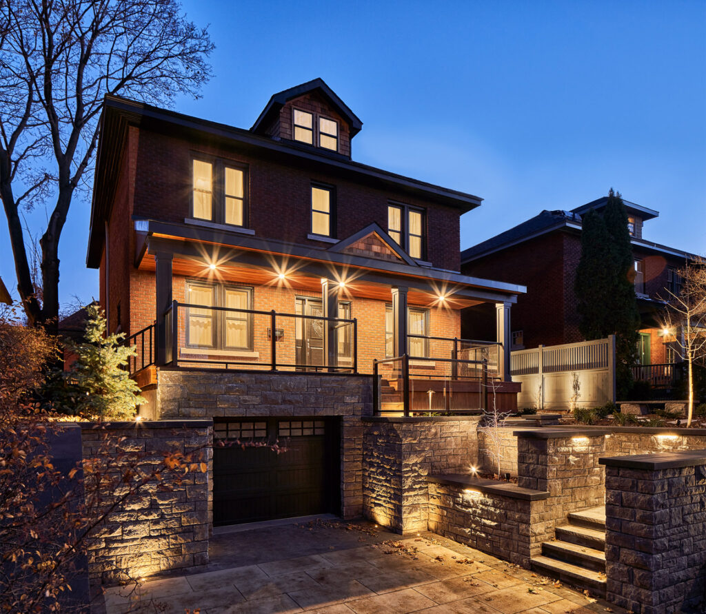 View of a renovated two-story brick home with illuminated exterior lighting and stone landscaping