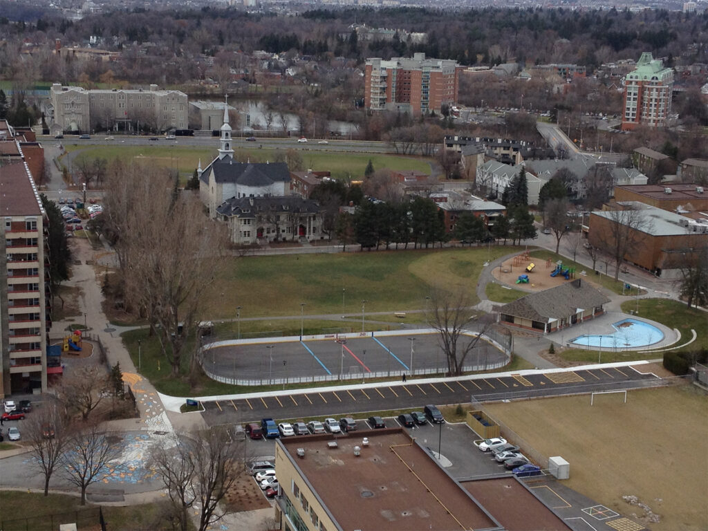 Aerial view of Jules Morin Park showing a circular concrete area, playground, parking lot, and surrounding buildings