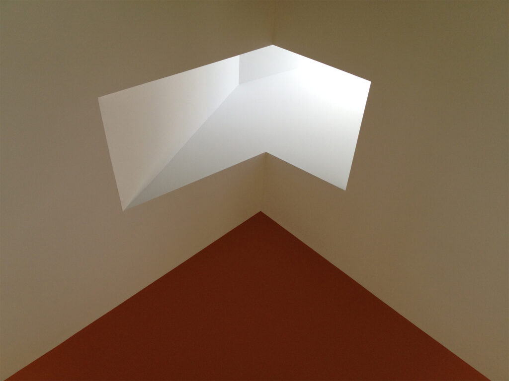 A geometric ceiling skylight casting natural light into a room with white walls and a contrasting orange accent wall
