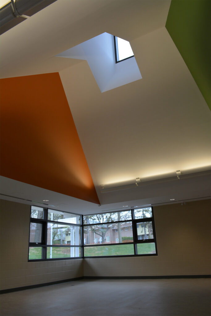 A room with geometric ceiling design featuring a skylight, orange and green walls, track lighting, and large windows with a view of the exterior