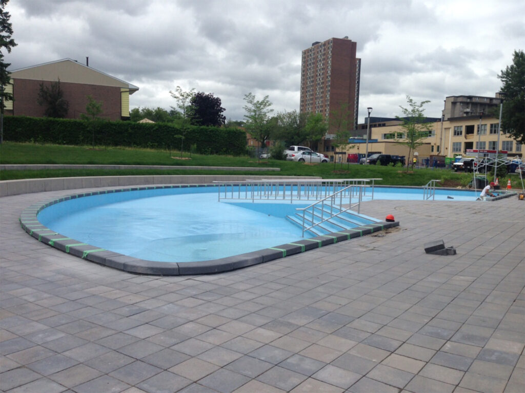 This image shows a close-up view of the circular pool at Jules Morin Park, with paved surrounds and a railing for safety
